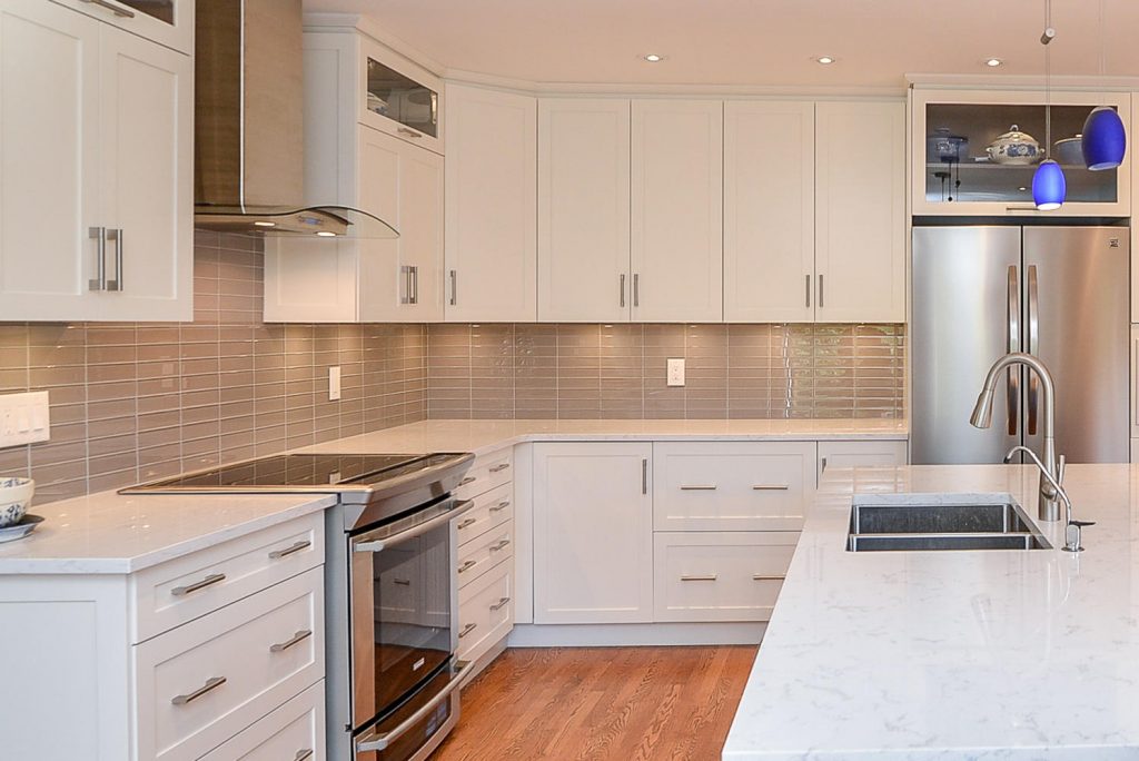 Modern kitchen featuring white cabinetry, gray backsplash, stainless steel appliances, and a marble countertop with a double sink.