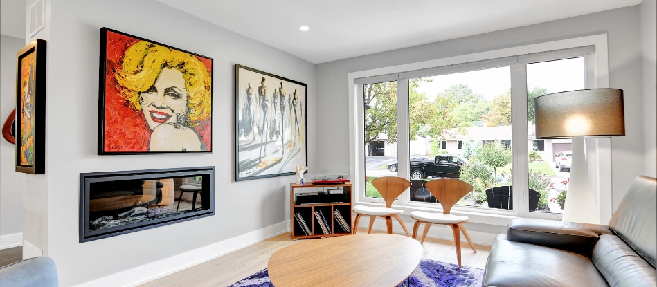 Modern living room with large window, colorful pop art portrait, and abstract painting. Features sleek furniture, wooden chairs, and cozy ambiance.