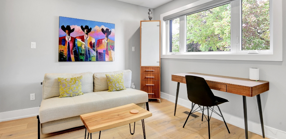 Minimalist room with a beige sofa, colorful abstract painting, wooden coffee table, and sleek desk under a large window