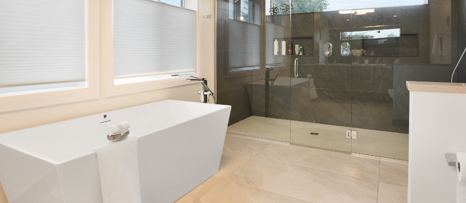 Modern bathroom with a sleek white bathtub beside large windows, and a spacious glass-enclosed shower area. Neutral tones convey a serene, minimalist vibe.